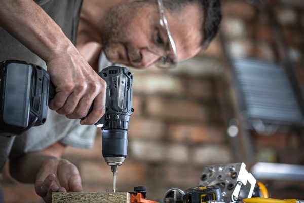 Screwing a self-tapping screw into a metal fastening hole on a wood strip using a screwdriver, the work of a carpenter.