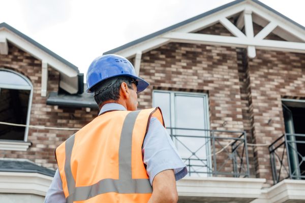Rear view of an American Indian national worker with a vest and hard hat on the construction site. looks at and inspects the building, the house,